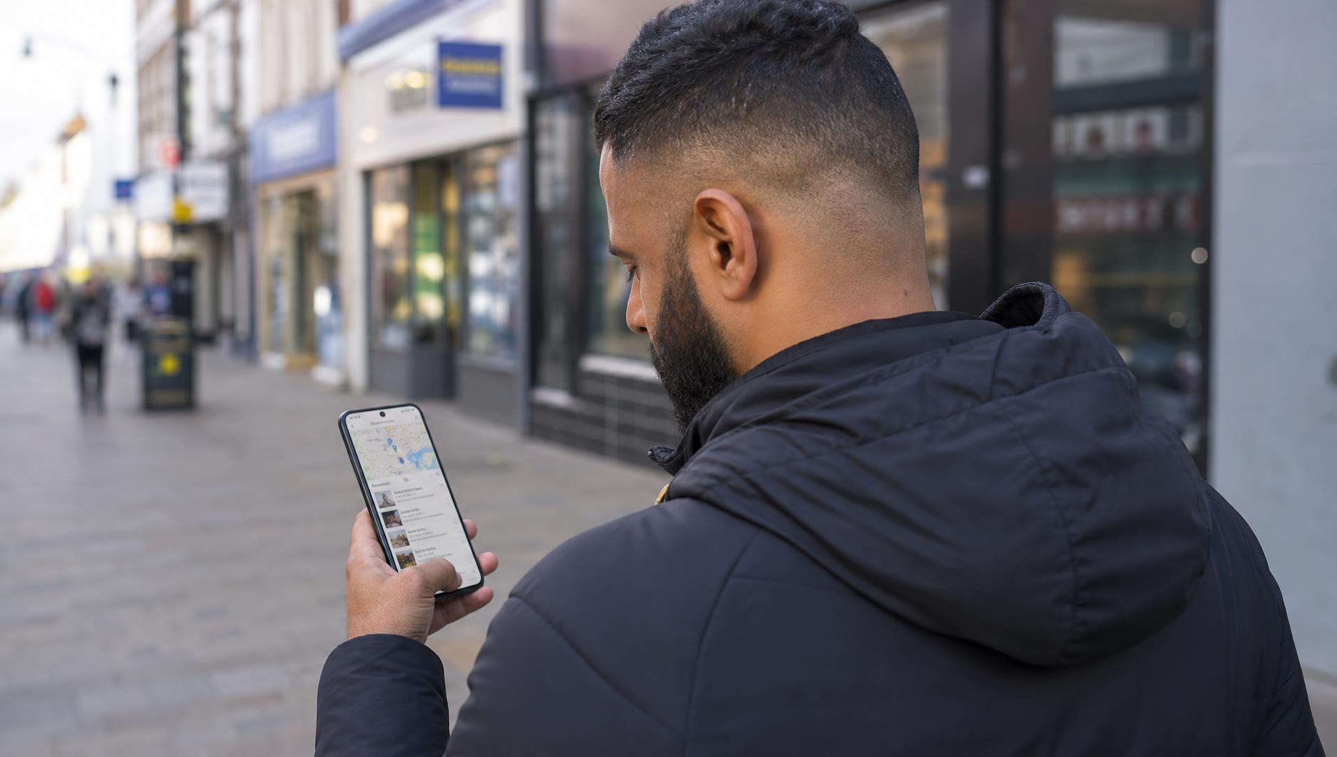 Customer on a British high street pavement looking up local businesses on their phone