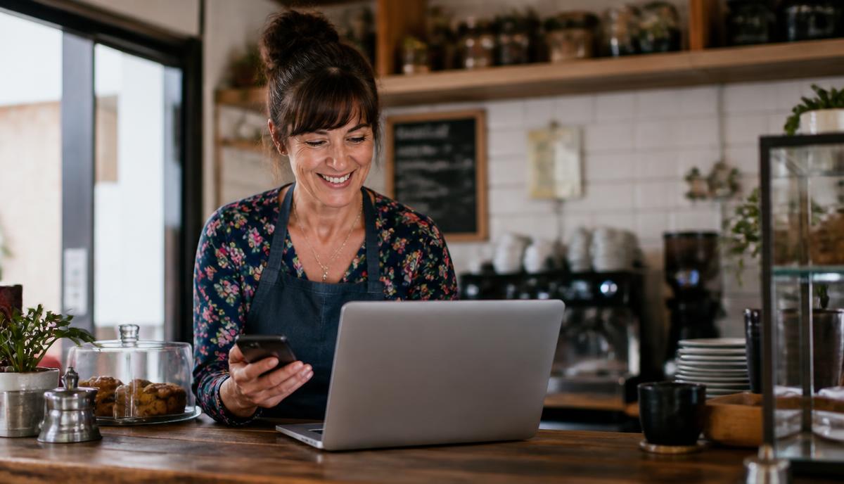 Small business owner behind a counter with a phone and laptop, using both social media and their own website